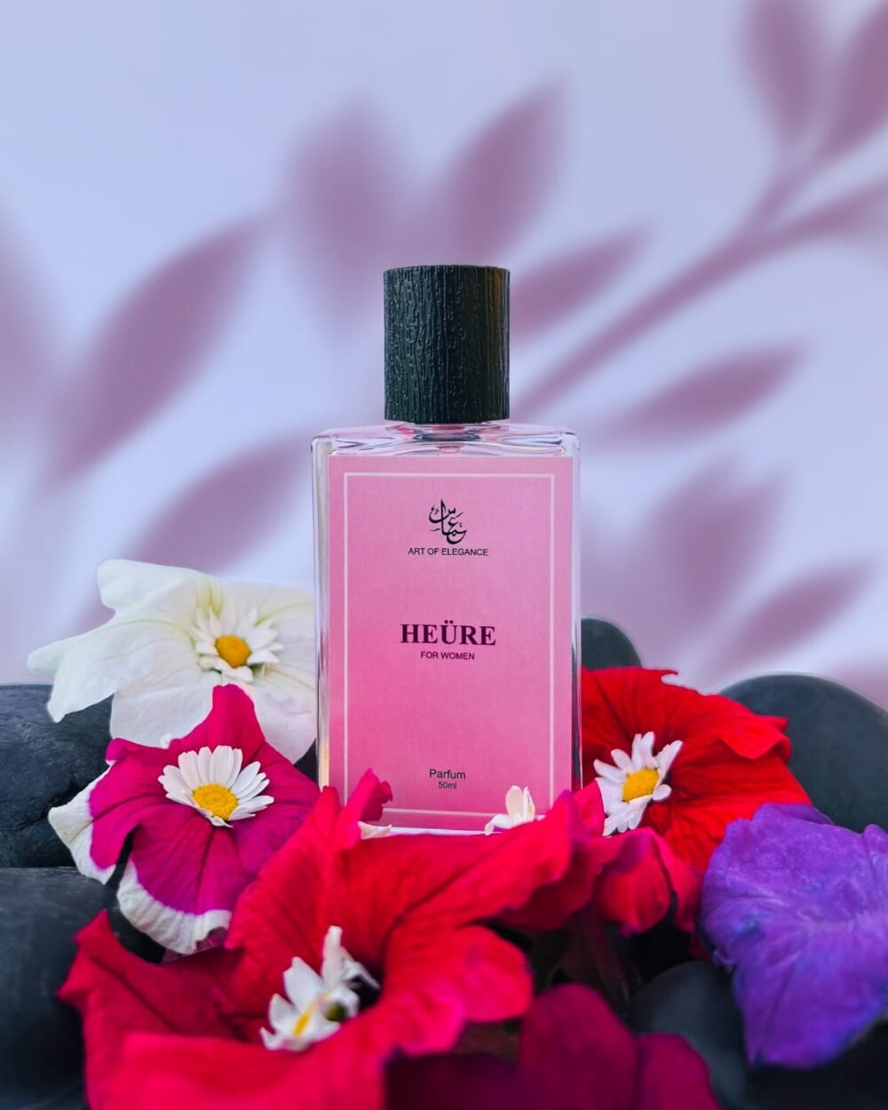 Pink bottle of “Heüre for Women” perfume by Art of Elegance, placed among vibrant flowers with a soft lavender leaf-shadowed background