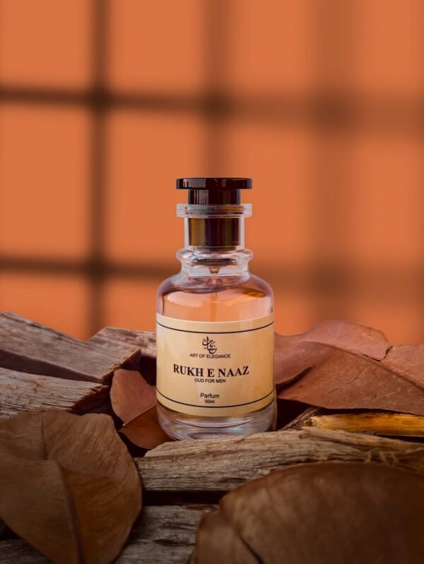 A premium glass bottle of “Rukh e Naaz – Oud for Men” perfume placed on rustic wooden planks with dried brown leaves, against a warm orange window-lit background.