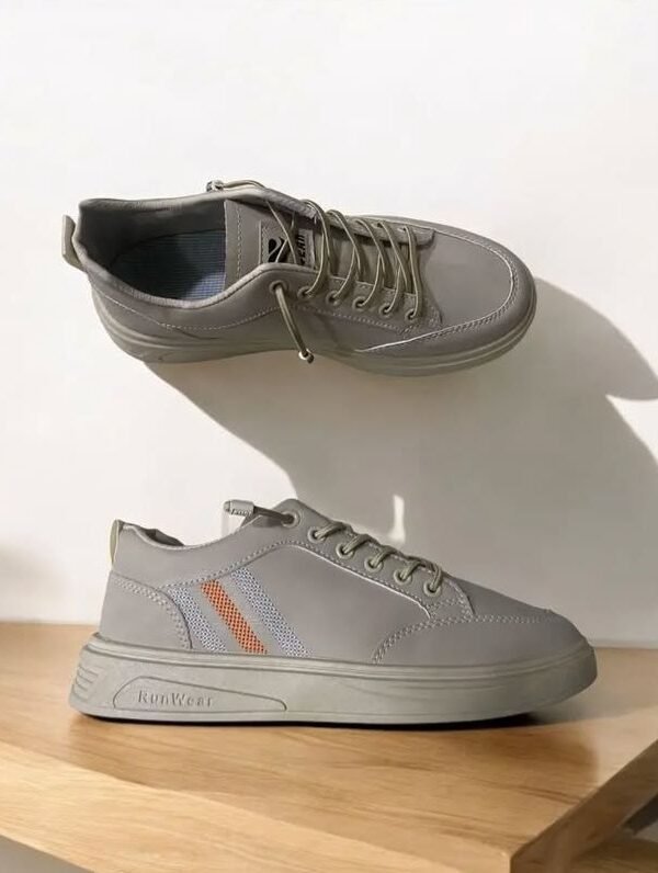 A pair of light grey sneakers with orange and grey mesh stripes displayed on a wooden surface in creative orientation with soft shadows in natural lighting.