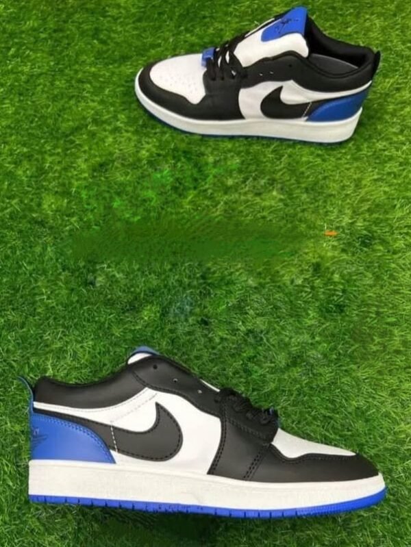 A pair of black, white, and blue low-top sneakers placed on vibrant artificial green grass, with one shoe lying flat and the other positioned above.