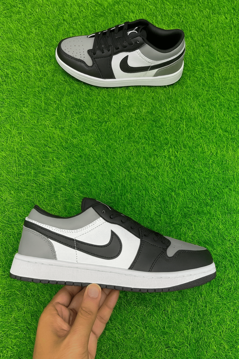 Black, white, and grey low-top sneakers displayed on vibrant artificial green grass, with one shoe lying flat and the other held in hand to showcase design details.
